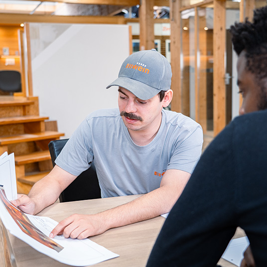 Ettwein-Mitarbeiter erklärt einem Kunden Baupläne am Besprechungstisch – persönliche Beratung und Planungskompetenz