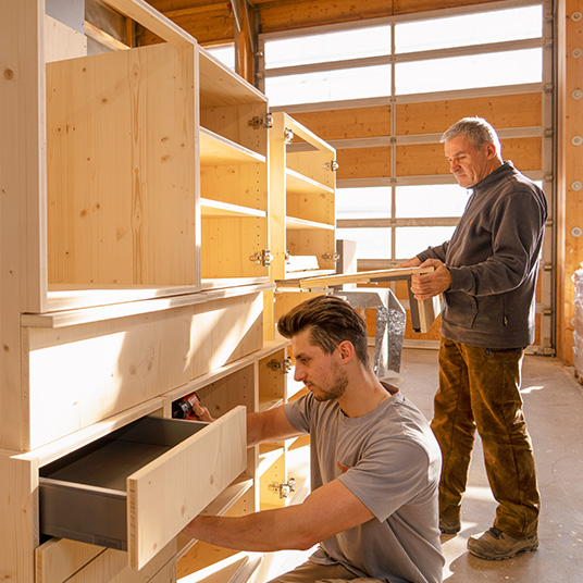 Zwei Mitarbeiter der Werner Ettwein GmbH fertigen in der Werkhalle einen maßgefertigten Holzschrank