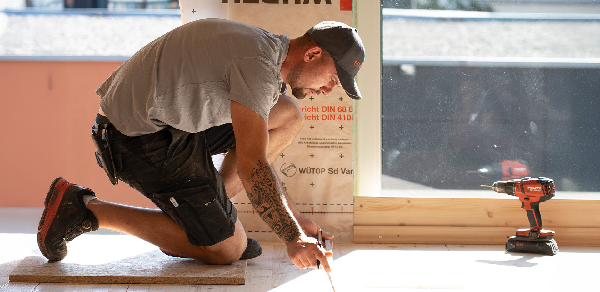 Mitarbeiter der Werner Ettwein GmbH misst auf einer Baustelle mit Zollstock den Boden aus, Akkuschrauber liegt bereit